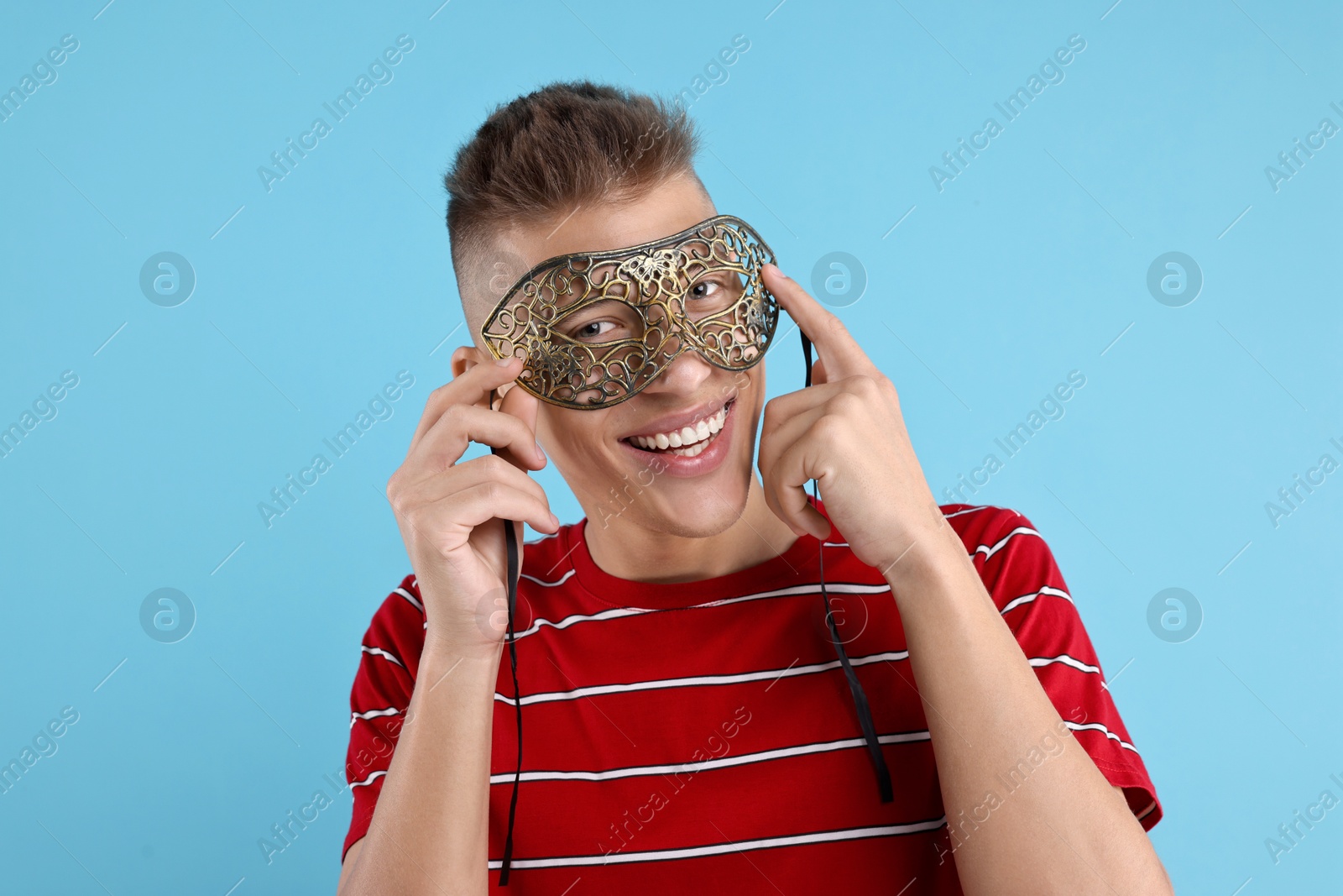 Photo of Charming young man wearing carnival mask on light blue background