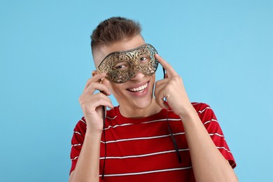 Charming young man wearing carnival mask on light blue background