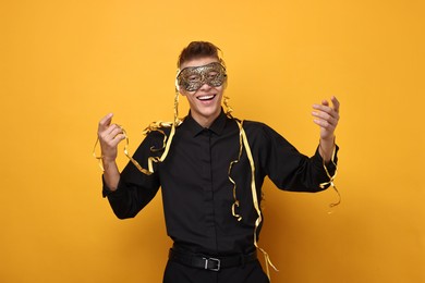 Charming young man wearing carnival mask on orange background