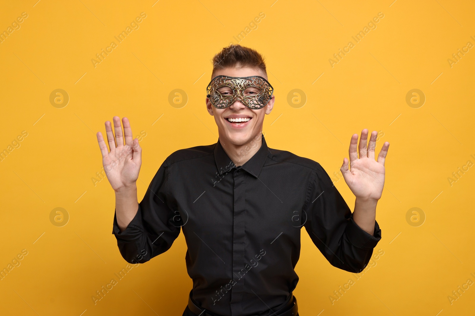 Photo of Charming young man wearing carnival mask on orange background