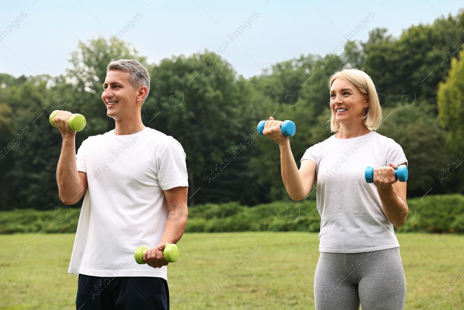 Photo of Happy couple doing exercise with dumbbells in park