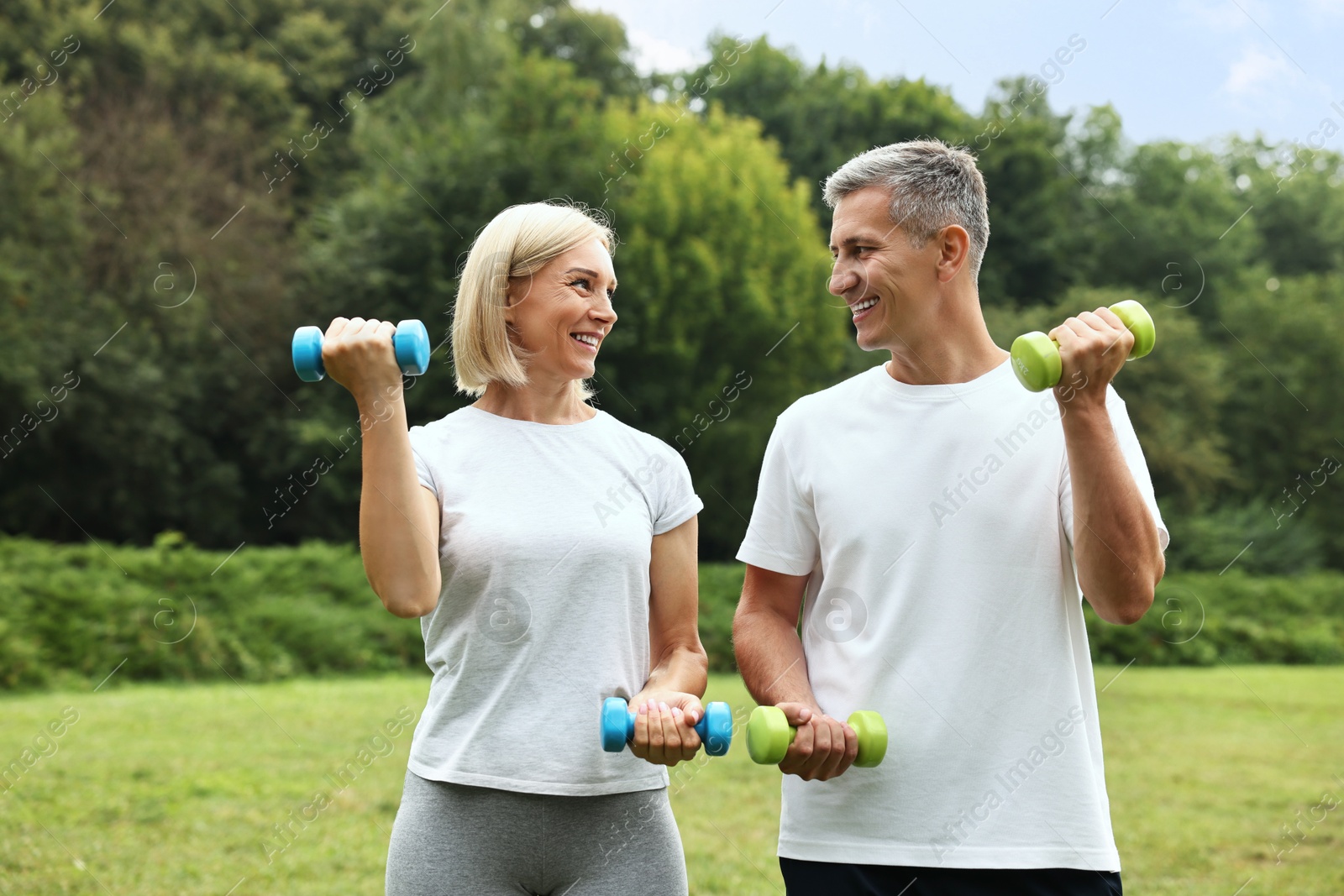 Photo of Happy couple doing exercise with dumbbells in park