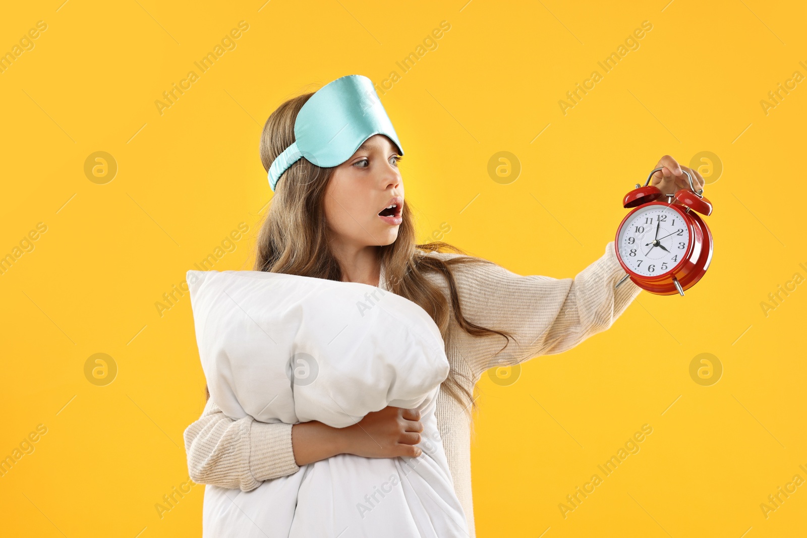 Photo of Overslept girl with sleep mask, pillow and alarm clock on orange background