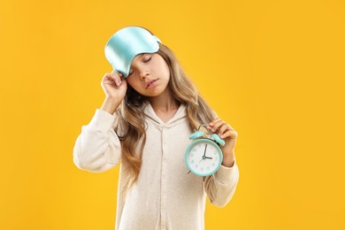 Photo of Overslept girl with sleep mask and alarm clock on orange background