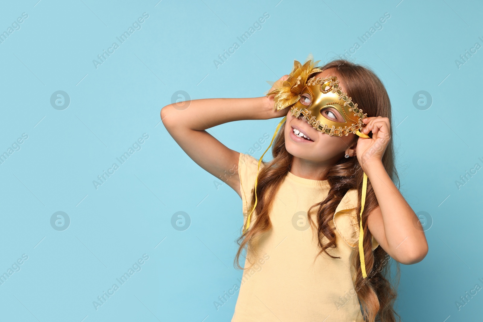 Photo of Happy girl wearing carnival mask on light blue background, space for text