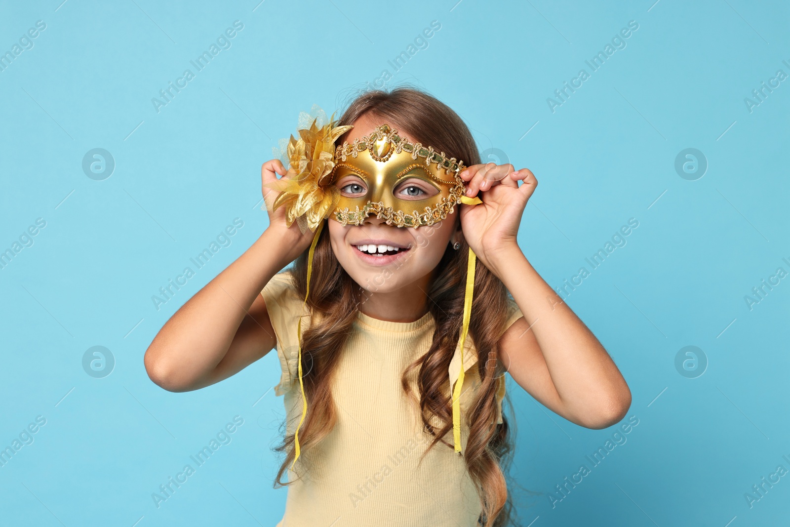 Photo of Happy girl wearing carnival mask on light blue background