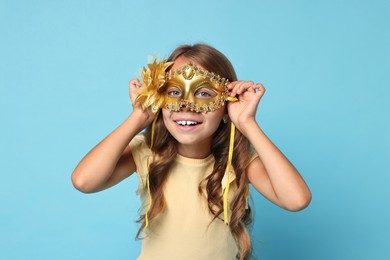 Photo of Happy girl wearing carnival mask on light blue background