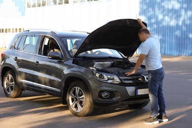 Photo of Stressed man looking under hood of broken car outdoors