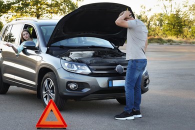 Stressed man standing near broken car while woman sitting in auto outdoors