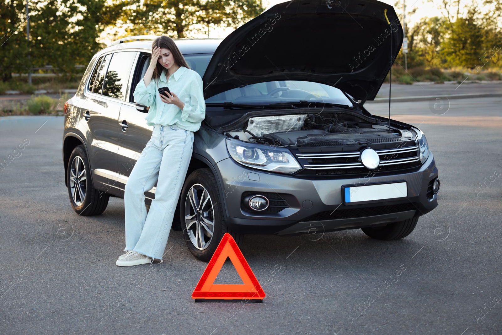 Photo of Stressed woman using smartphone near broken car outdoors