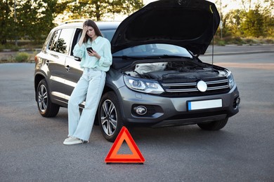 Photo of Stressed woman using smartphone near broken car outdoors