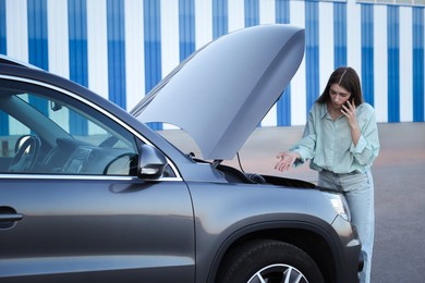 Stressed woman talking on phone near broken car outdoors