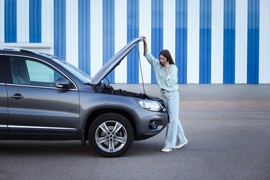 Stressed woman talking on phone near broken car outdoors