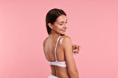 Smiling woman with cream on shoulder against pink background. Body care