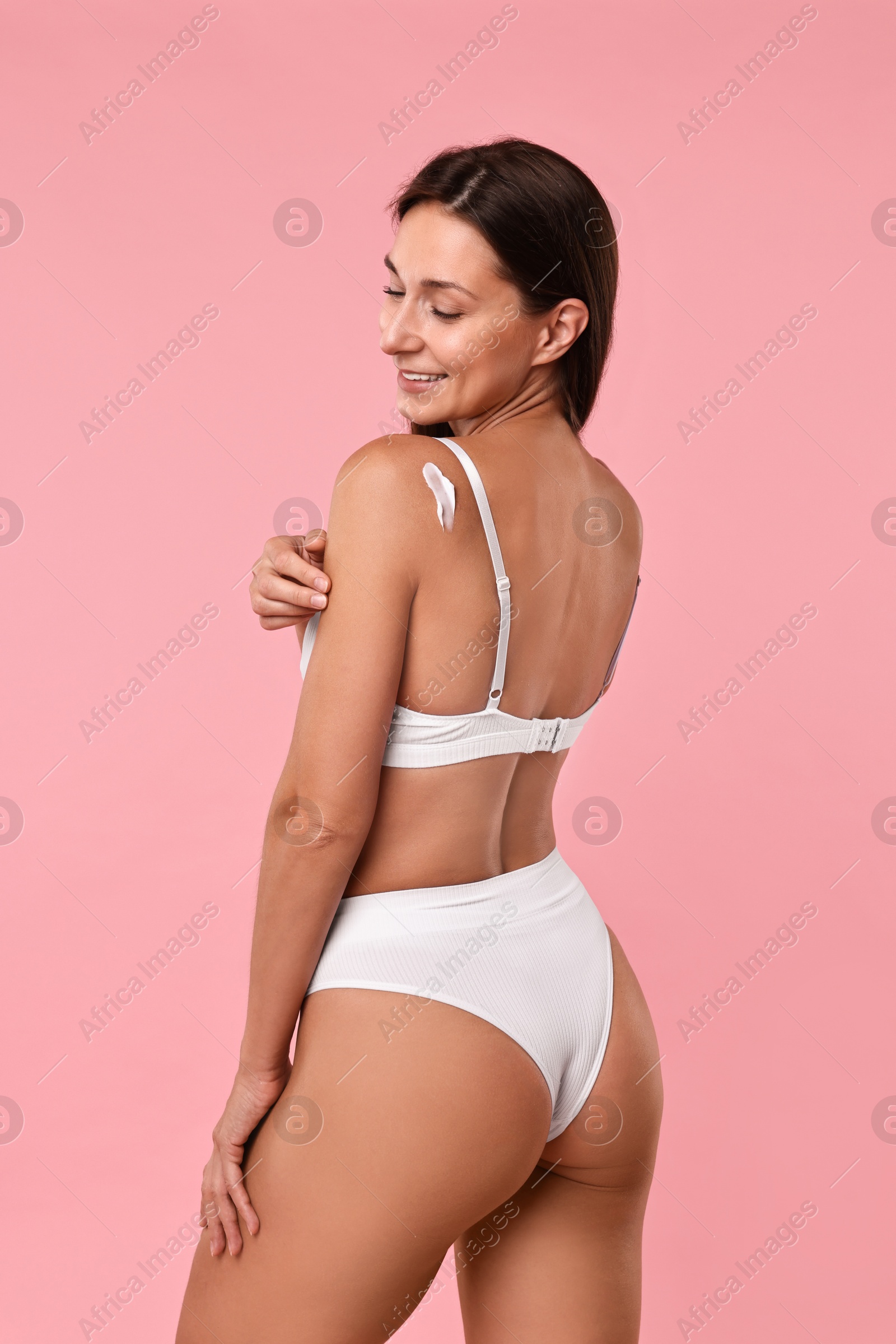 Photo of Smiling woman with cream on shoulder against pink background. Body care