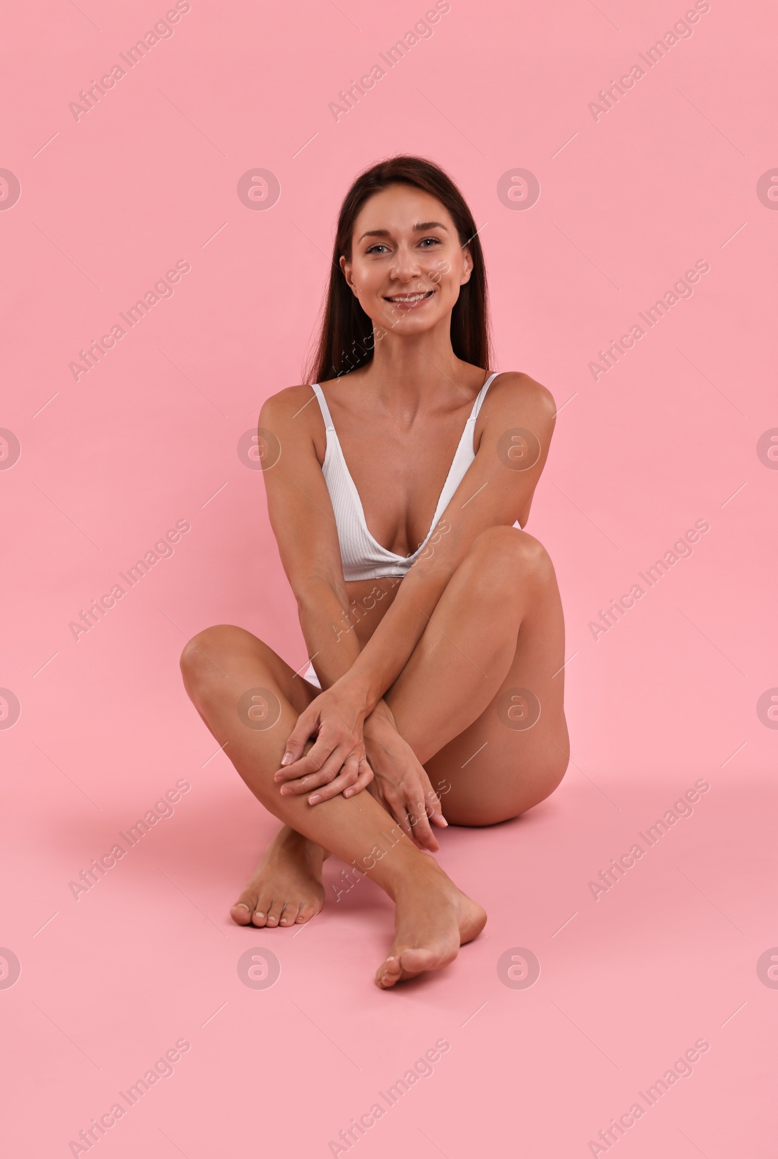 Photo of Smiling woman with perfect skin sitting on pink background. Body care