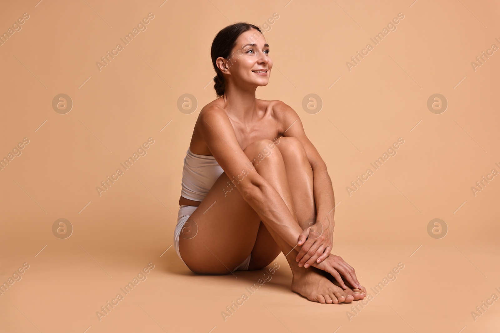 Photo of Smiling woman with perfect skin sitting on beige background. Body care