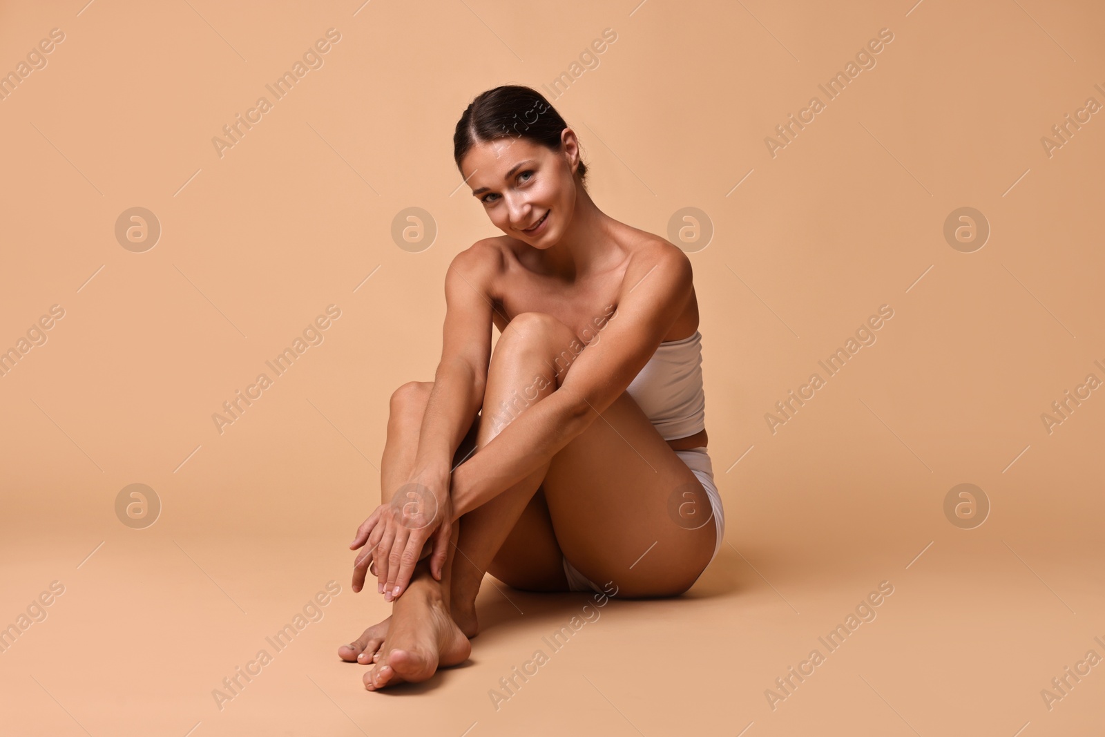 Photo of Smiling woman with perfect skin sitting on beige background. Body care