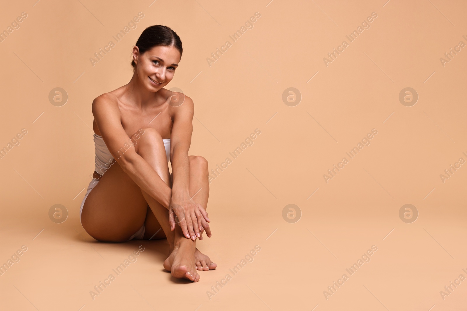 Photo of Smiling woman with perfect skin sitting on beige background, space for text. Body care