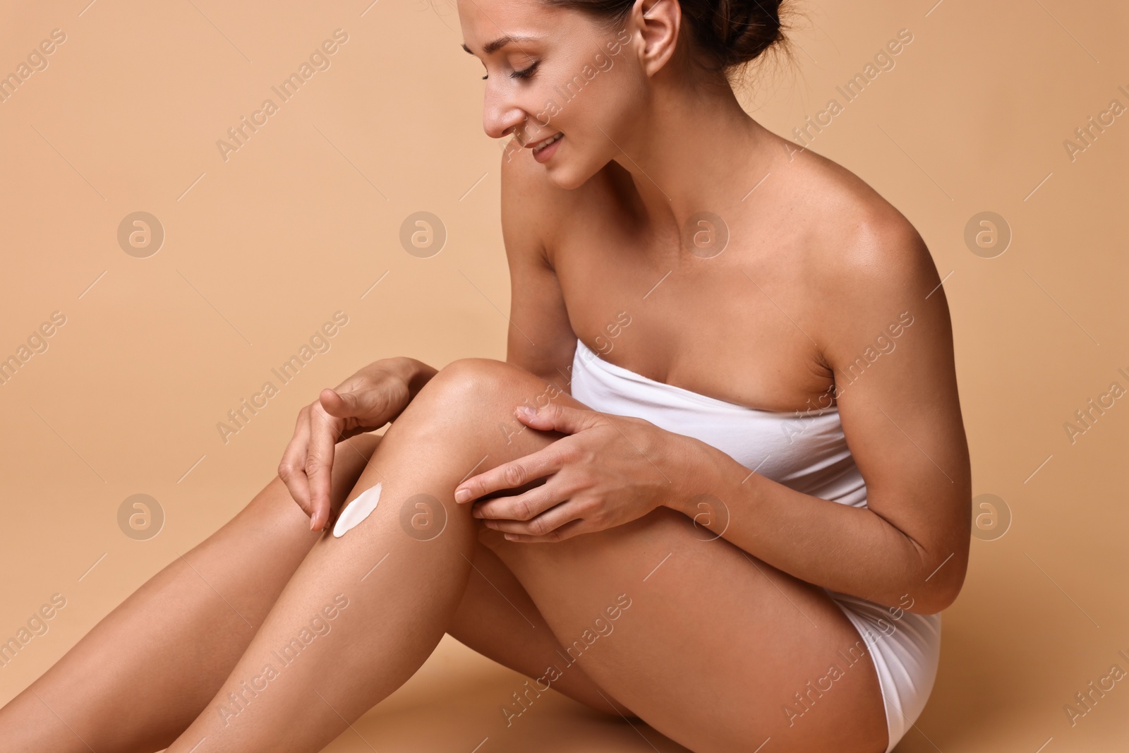 Photo of Beautiful woman applying cream onto leg against beige background. Body care