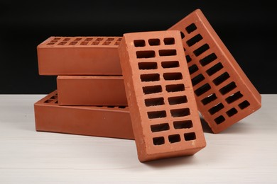 Photo of Many red bricks on light wooden table against black background. Building material