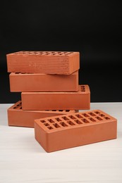 Many red bricks on light wooden table against black background. Building material