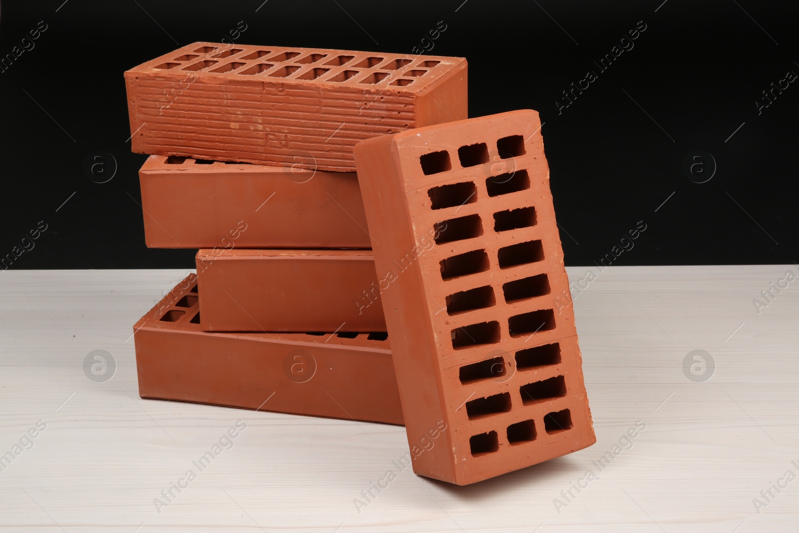 Photo of Many red bricks on light wooden table against black background. Building material