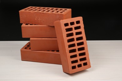 Many red bricks on light wooden table against black background. Building material