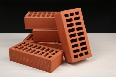 Photo of Many red bricks on light wooden table against black background. Building material