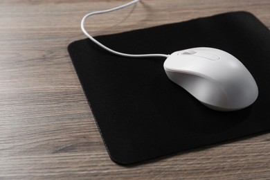 Photo of Computer mouse with mousepad on wooden table, closeup