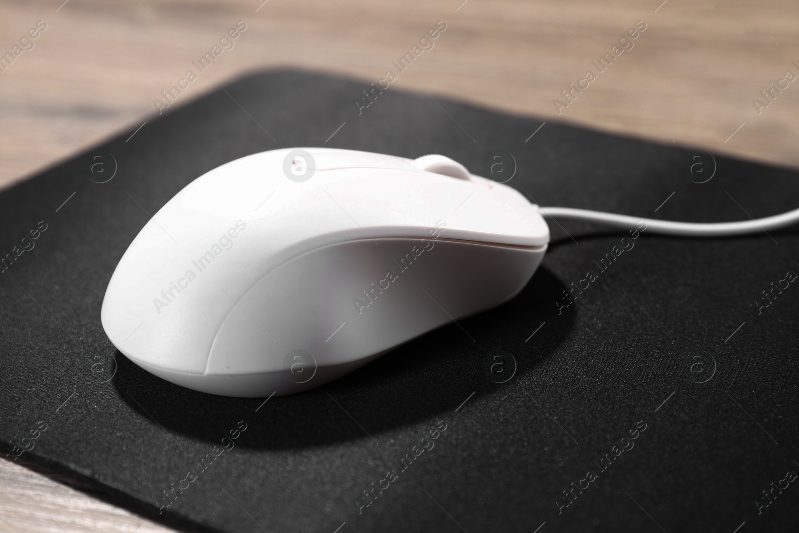 Photo of Computer mouse with mousepad on wooden table, closeup