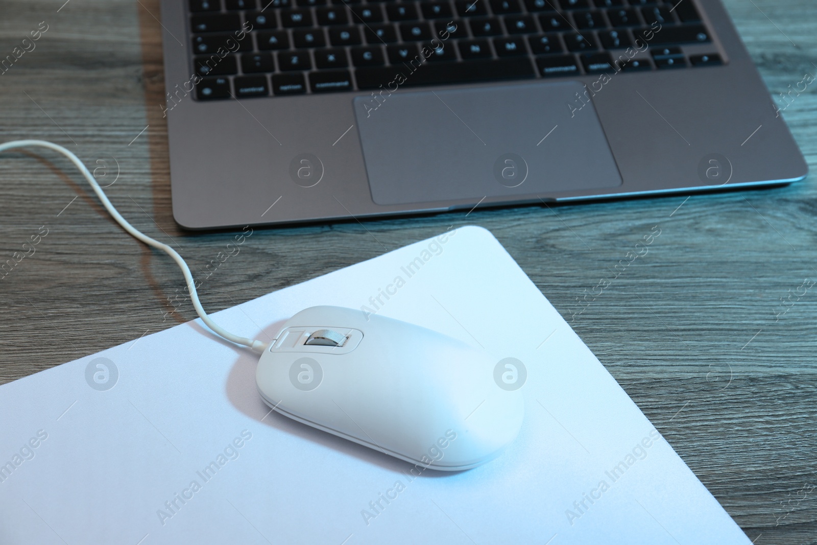 Photo of Computer mouse with mousepad and laptop on wooden table