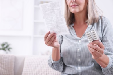 Senior woman with pills reading medicine instruction at home, closeup. Space for text