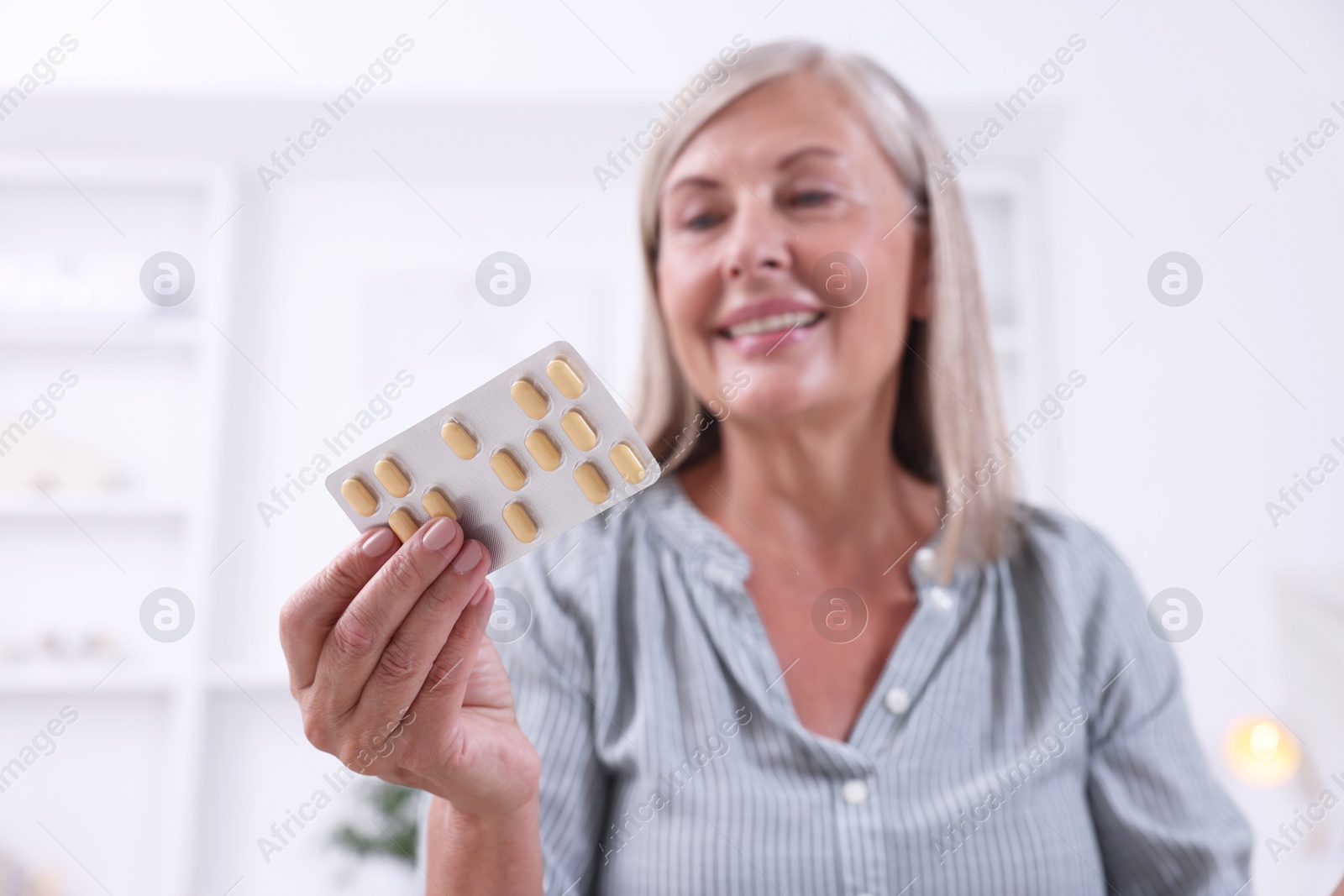 Photo of Senior woman holding blister with pills at home, selective focus