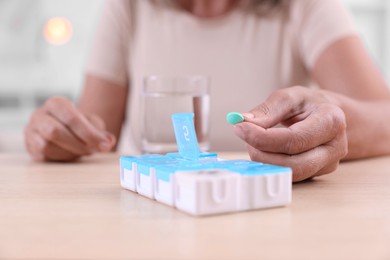 Photo of Senior woman taking pill from organizer at table indoors, closeup