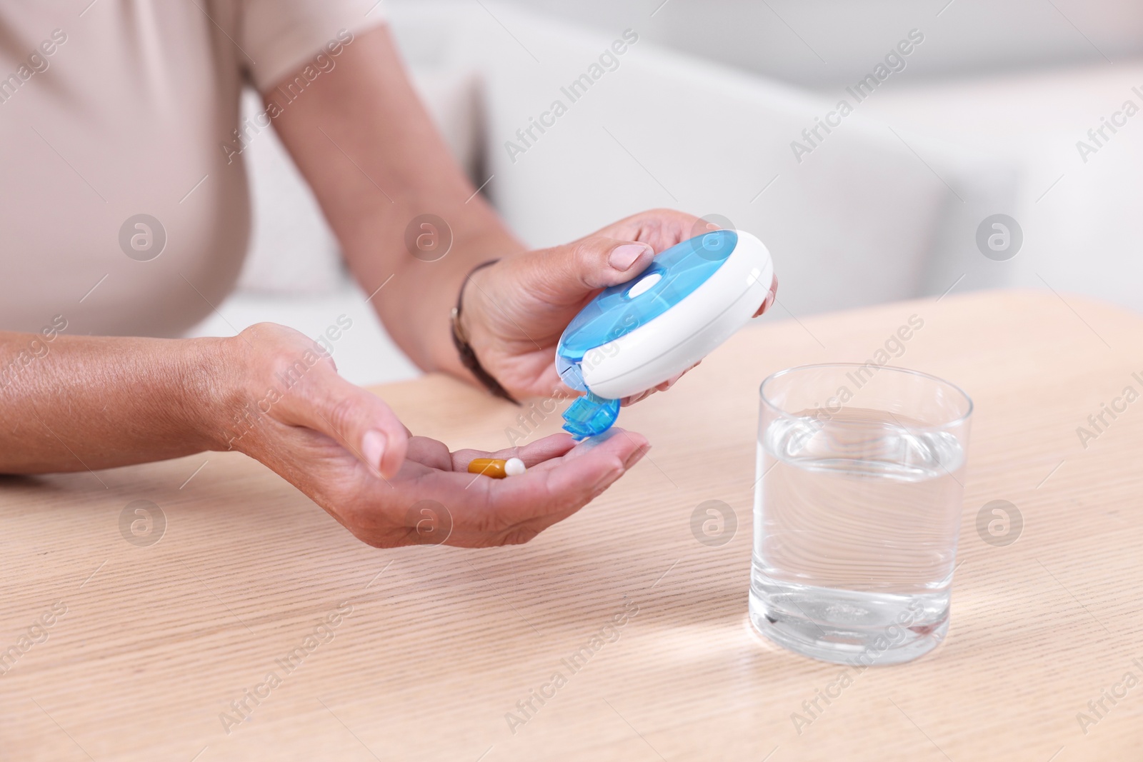 Photo of Senior woman pouring pills from organizer into hand at table indoors, closeup