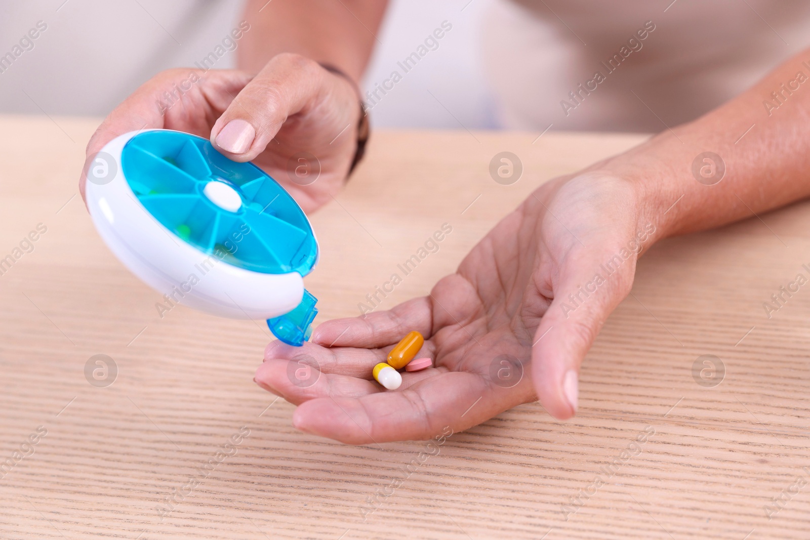 Photo of Senior woman pouring pills from organizer into hand at table indoors, closeup