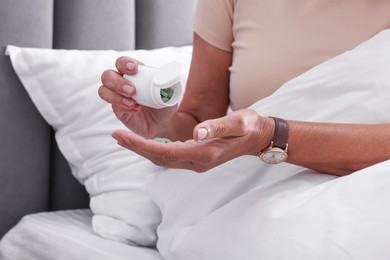 Senior woman pouring pills from bottle into hand in bed at home, closeup