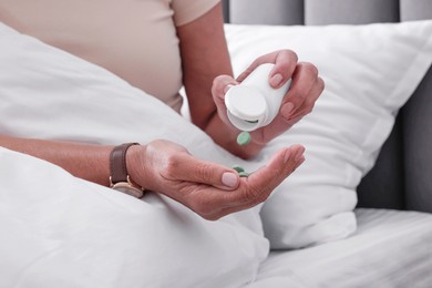 Photo of Senior woman pouring pills from bottle into hand in bed at home, closeup