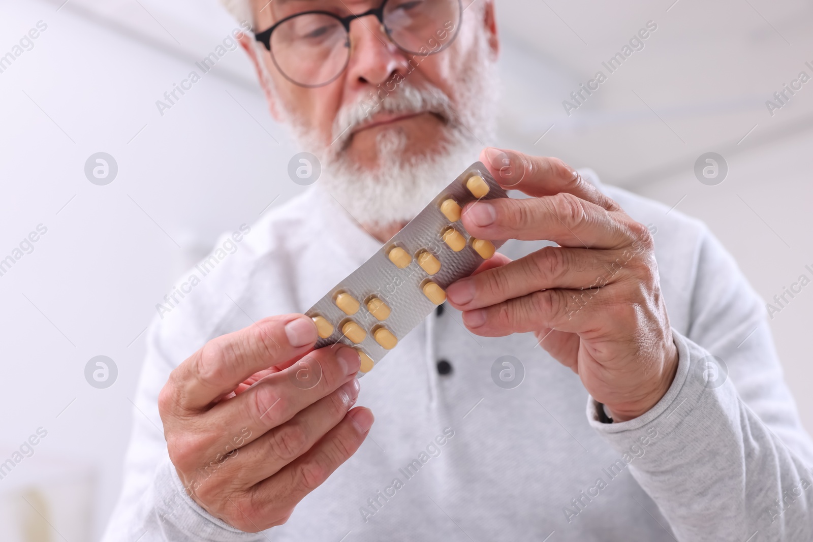 Photo of Senior man holding blister with pills at home, selective focus