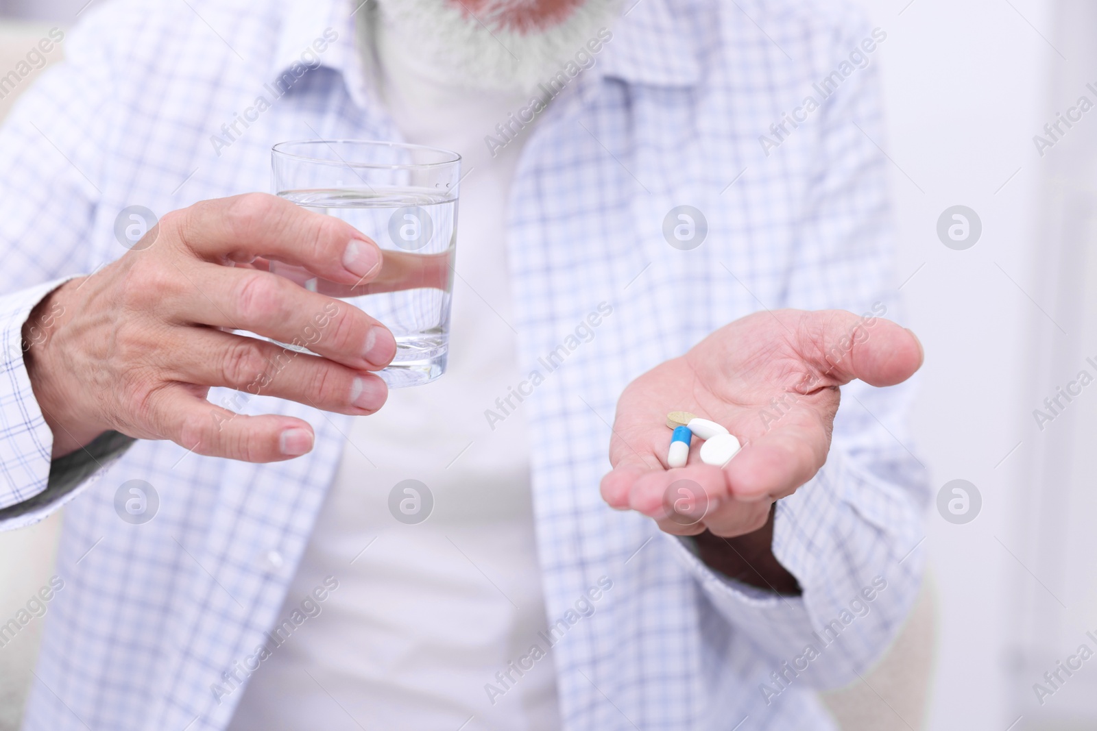 Photo of Senior man with glass of water and pills at home, closeup