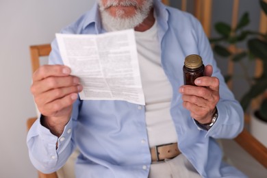 Senior man with pills reading medicine instruction at home, closeup