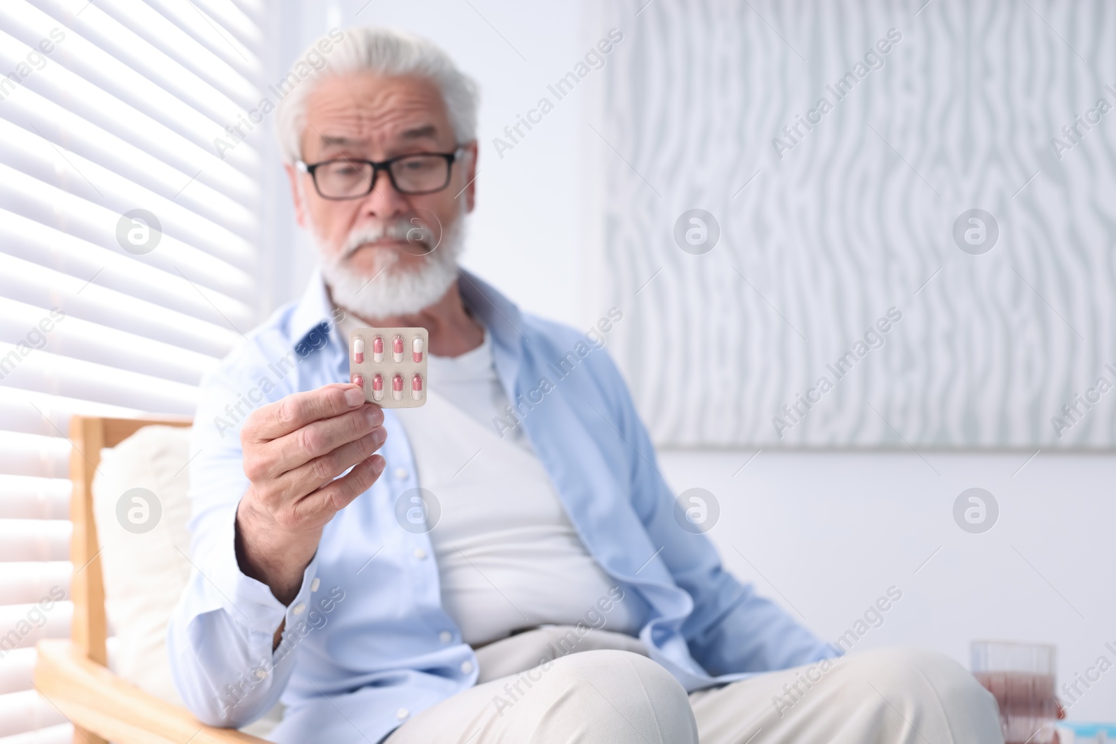 Photo of Senior man holding blister with pills at home, space for text