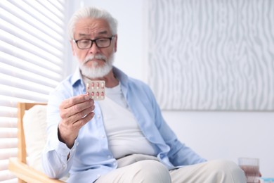 Senior man holding blister with pills at home, space for text