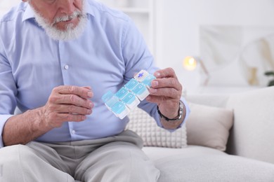 Photo of Senior man with pill organizer on sofa at home, closeup