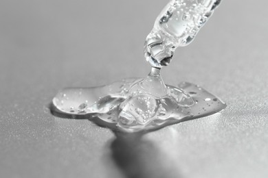 Photo of Dripping cosmetic serum from pipette on grey background, closeup