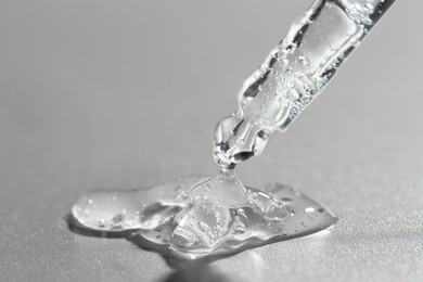 Photo of Dripping cosmetic serum from pipette on grey background, closeup