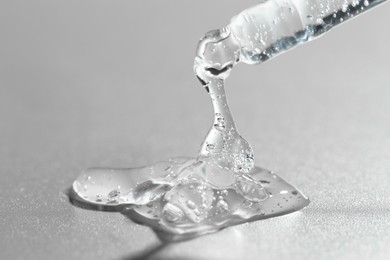 Photo of Dripping cosmetic serum from pipette on grey background, closeup