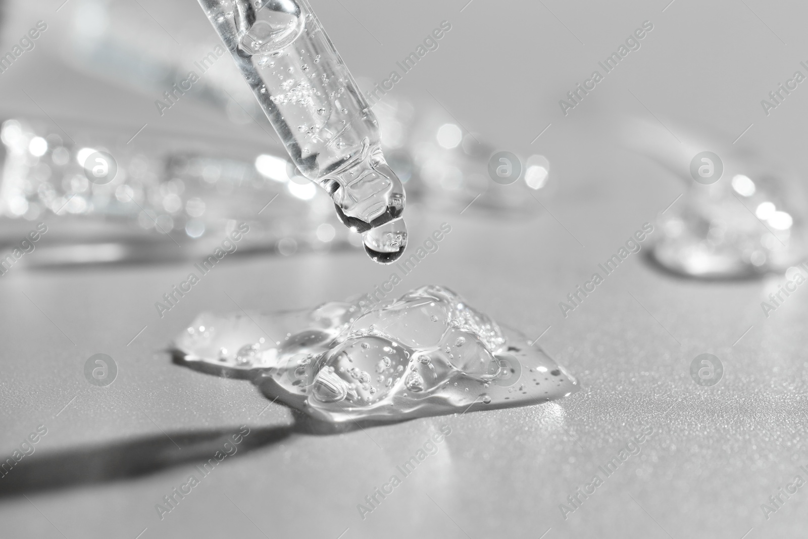 Photo of Dripping cosmetic serum from pipette on grey background, closeup