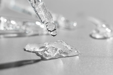 Photo of Dripping cosmetic serum from pipette on grey background, closeup